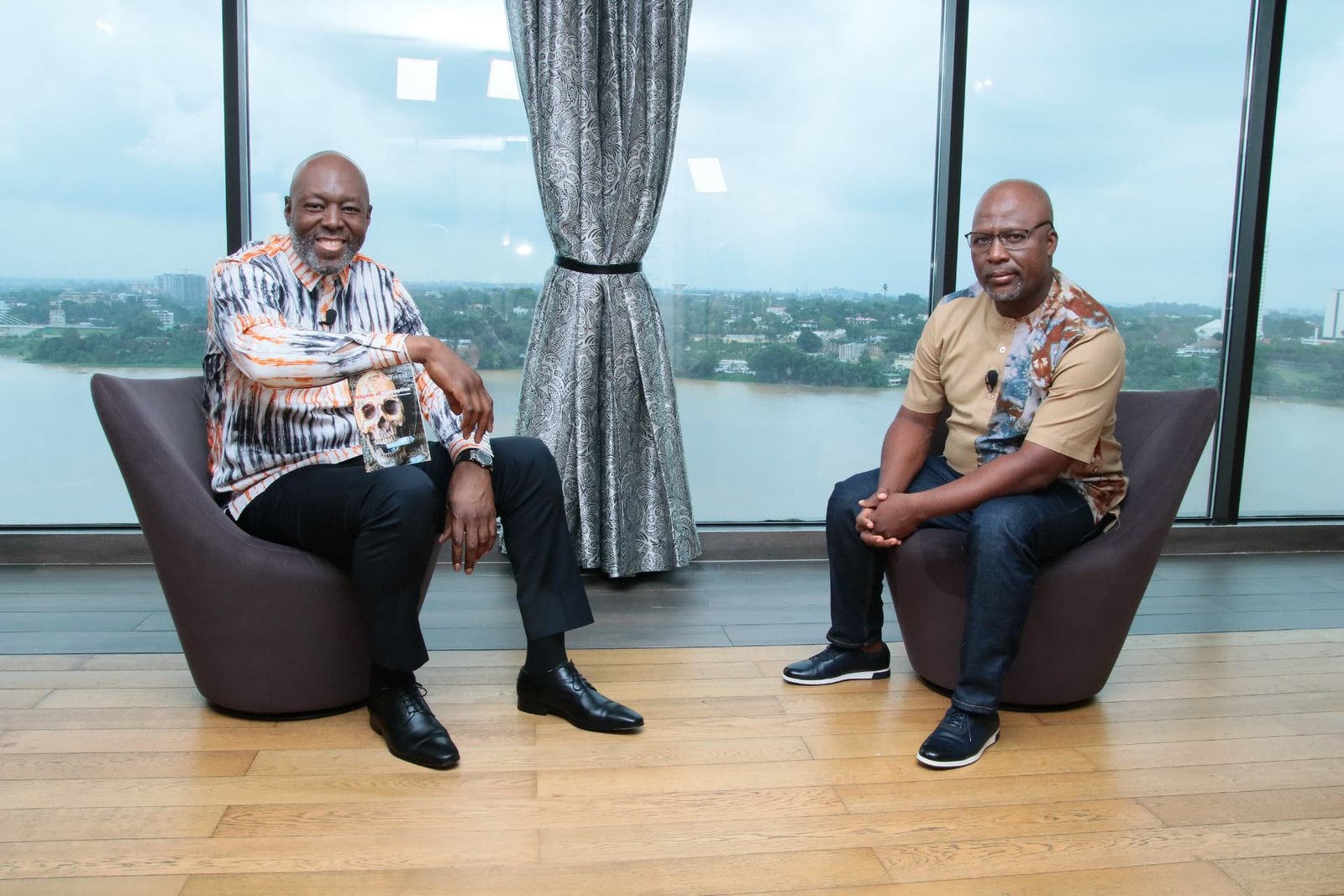 Robert Brazza en tournage face à son invité, baie vitrée sur la lagune d'Abidjan
